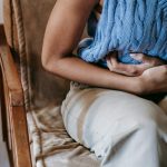Person sitting on chair, clutching their abdomen in pain.