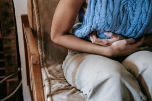 Person sitting on chair, clutching their abdomen in pain.